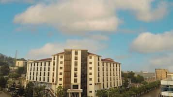 A multi-story hotel with a central atrium, surrounded by a street with parked cars and trees.