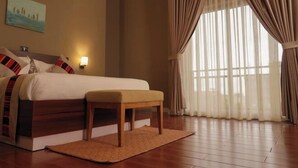A neatly made bed with a wooden bench, a nightstand with a lamp, and a large window with sheer curtains. - Haile Hotel Wolaita (Sodo)