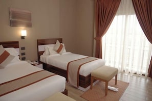 Habitación de hotel con dos camas, una mesita de noche, un escritorio, una silla y una ventana con cortinas.