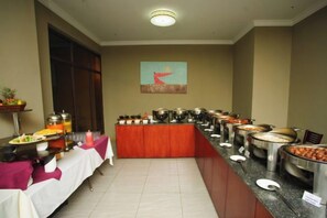 A buffet setup with multiple food stations, a table with a white tablecloth, and a painting on the wall.