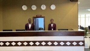 A reception desk with two staff members, a clock, and a reception sign. - Haile Hotel Wolaita (Sodo)