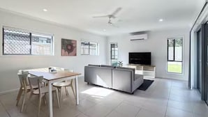 Una sala de estar moderna con comedor, un sofá, un televisor y ventanas amplias.