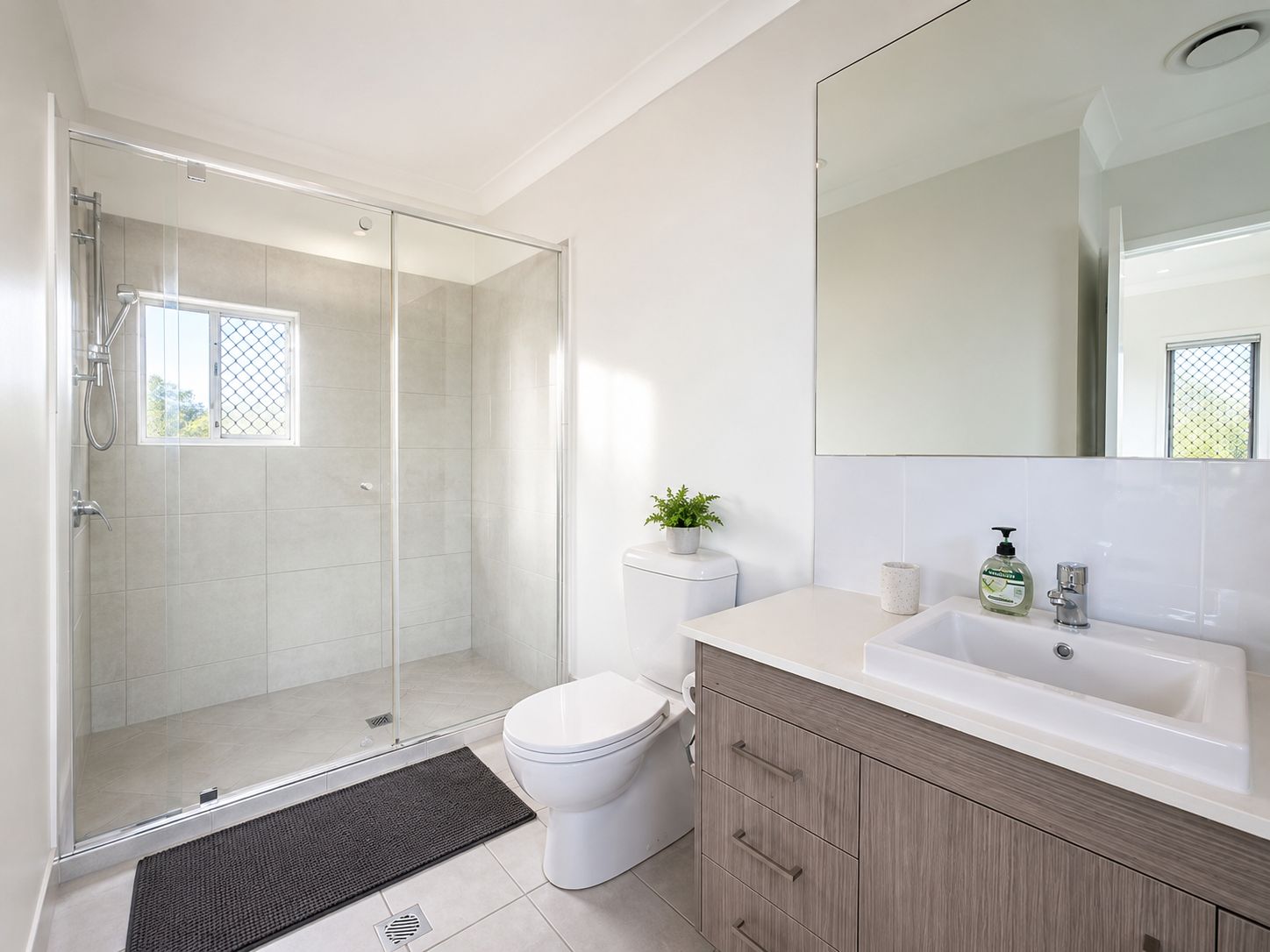 A modern bathroom with a glass shower enclosure, a toilet, a sink, and a mirror.