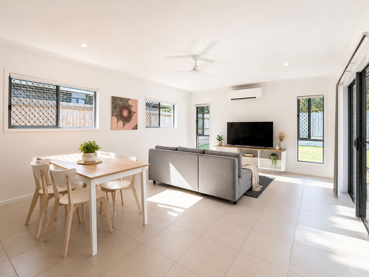 A modern living room with a sofa, TV, and dining area with chairs and a table.