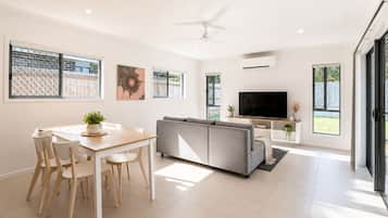 A modern living room with a sofa, TV, and dining area with chairs and a table.