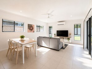 A modern living room with a sofa, TV, and dining area with chairs and a table.