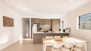 A modern kitchen with a central island, white cabinetry, and a dining area with a wooden table and chairs. - Sparkling New Home - Suburban Charms Awaits (Park Ridge)