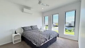 Un dormitorio con cama, mesita de noche, ventilador de techo y ventanas amplias.