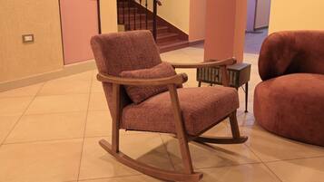 A rocking chair in a room with a tiled floor, a staircase in the background, and a small table with a basket.