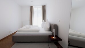 Moderni hotellihuone, jossa on siististi pedattu sänky, yöpöytä lampun kanssa ja suuri peili seinällä.