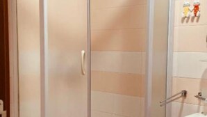 Un espace de douche d’angle avec une porte en verre, un lavabo blanc et un mur carrelé.