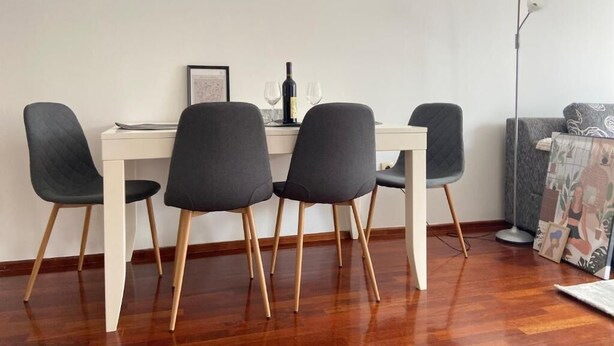 Un coin repas avec une table blanche, quatre chaises grises, une bouteille et des verres.