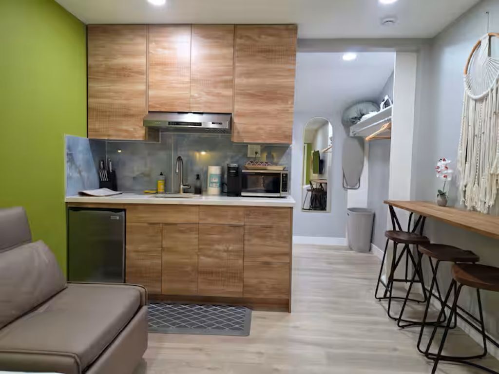 Une cuisine compacte avec des meubles en bois, un four à micro-ondes encastré et un petit réfrigérateur. On y trouve également un coin bar avec des tabourets et une décoration murale.