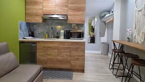 A compact kitchen with wooden cabinets, a built-in microwave, and a small refrigerator. There is a bar area with stools and a decorative wall hanging. - Private Urban Oasis Near SF - w/kitchenette 22421B (Hayward)