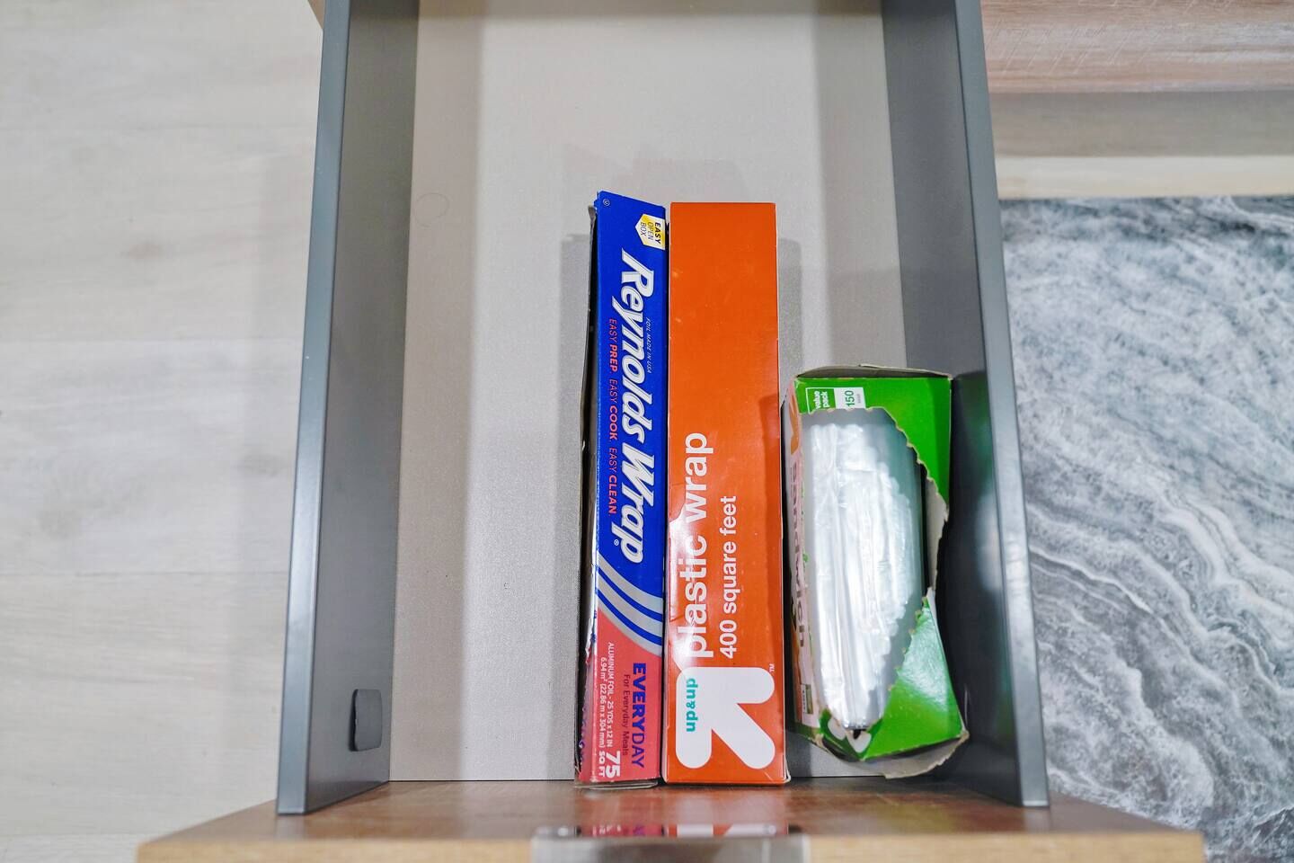 Een plank met twee dozen Reynolds Wrap en een groene doos plasticfolie.