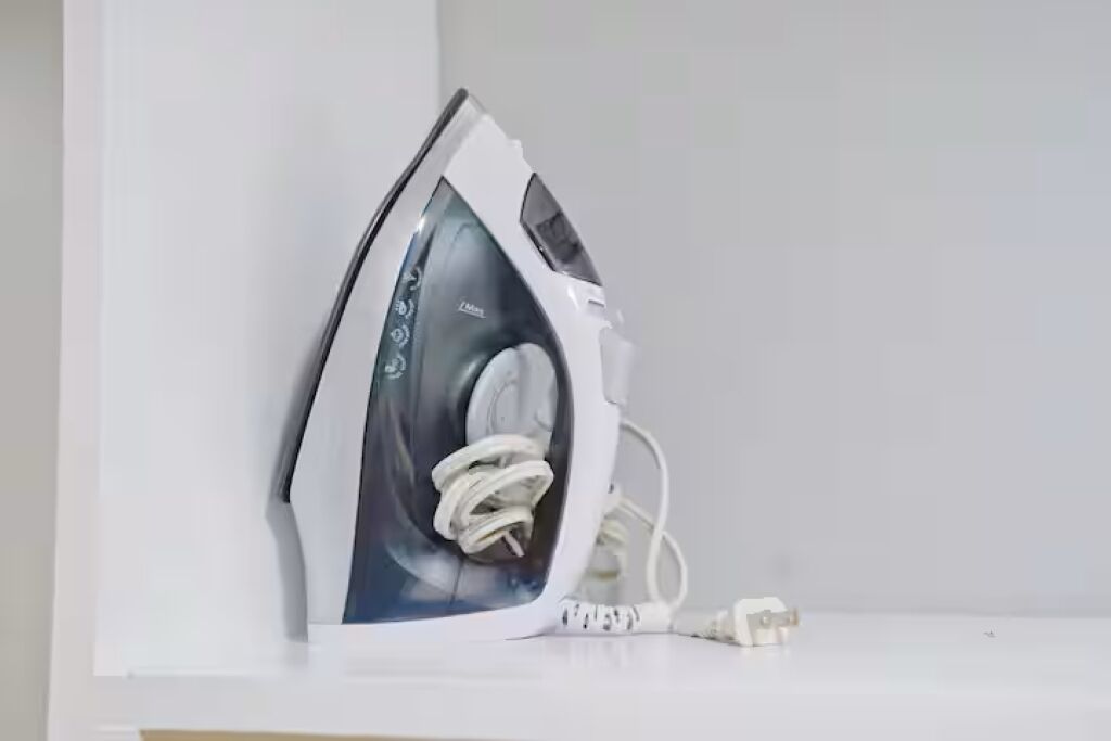 A white iron with a cord plugged in, placed on a white surface.