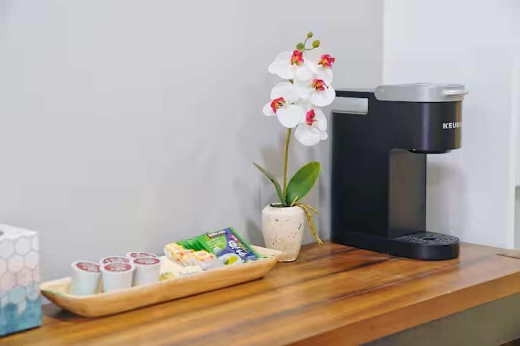 Eine Kaffeemaschine, ein Tablett mit Speisen und eine Topf-Orchidee auf einer Holztischfläche.