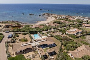 Vue aérienne d’un quartier résidentiel situé sur la côte, avec une piscine, des maisons à étages et un littoral rocheux.