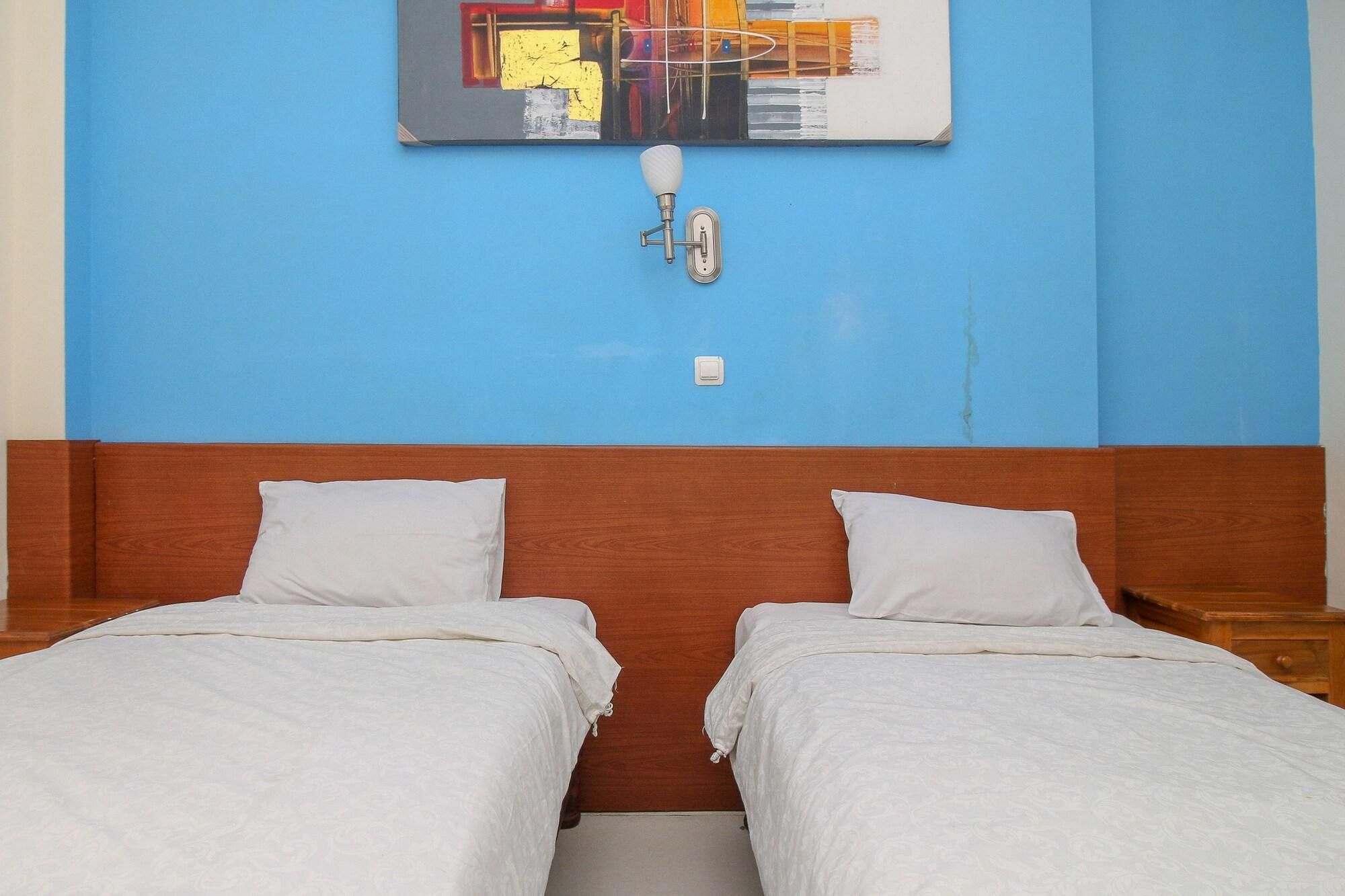 Una habitación con dos camas individuales, cabecero de madera, pared azul y un cuadro sobre las camas.