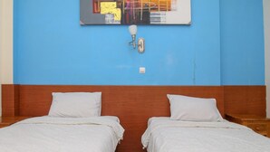 Una stanza con due letti singoli, una testiera in legno, una parete blu e un quadro sopra i letti.