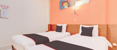 Habitación de hotel con dos camas, ropa de cama blanca con detalles rojos, cabecera de madera, una obra de arte colgada en la pared y un interruptor de luz.
