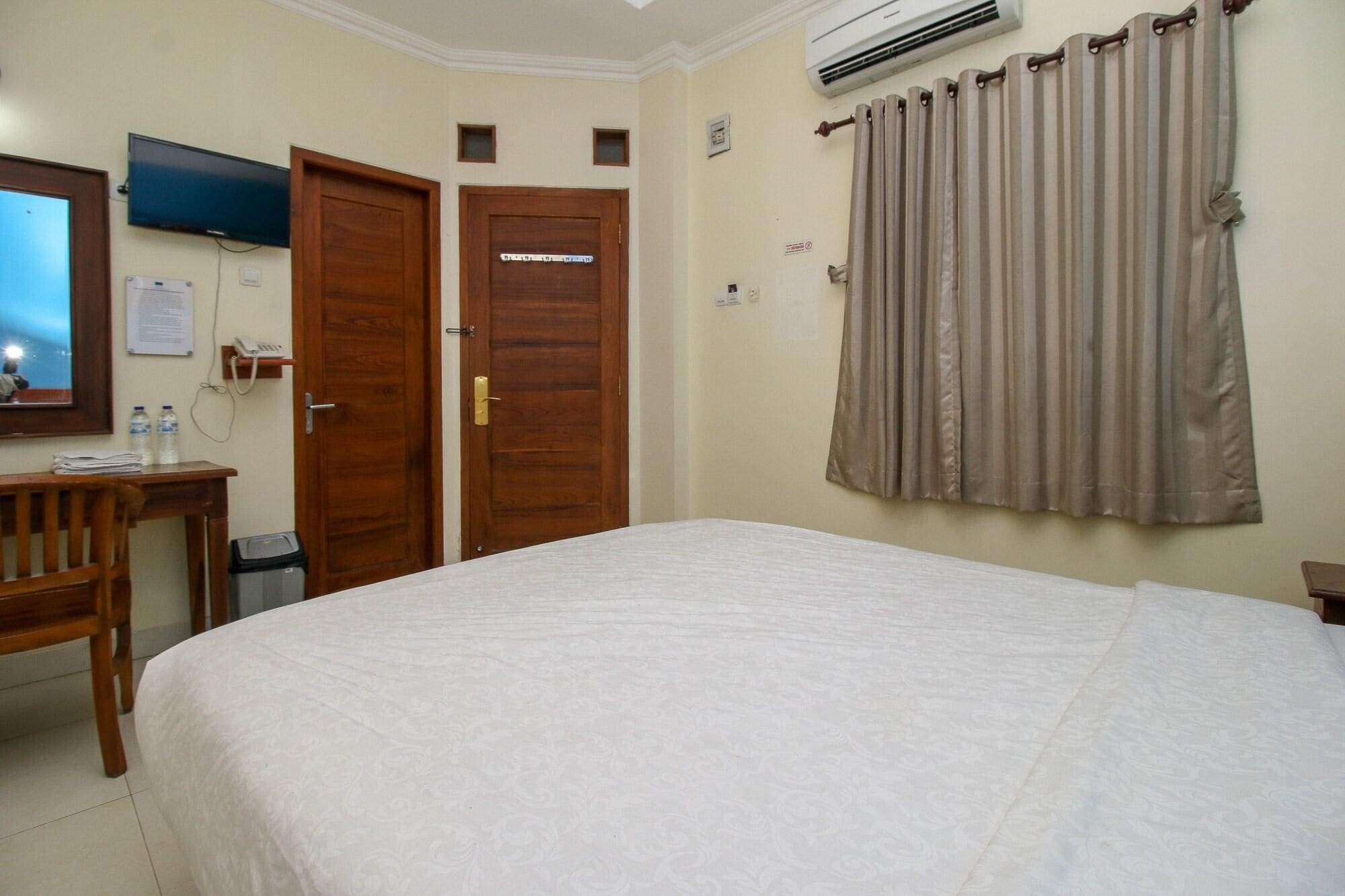 A hotel room with a bed, a desk, a chair, a television, and a window with curtains.