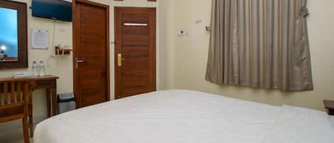 A hotel room with a bed, a desk, a chair, a television, and a window with curtains.