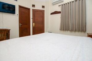 A bedroom with a large bed, two wooden doors, a wall-mounted air conditioner, and a curtain. - Collection O Jalan Malioboro Near Lempuyangan Stat (Yogyakarta)