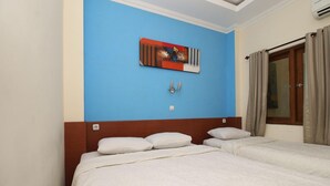 Una camera d'albergo con una parete di colore blu, un letto con biancheria bianca, una testiera in legno, un quadro e una finestra con tende.