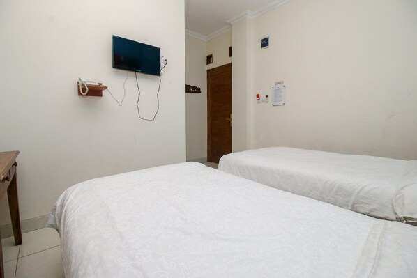 A hotel room with two beds, a TV mounted on the wall, a wooden door, and a small table. - Collection O Jalan Malioboro Near Lempuyangan Stat (Yogyakarta)