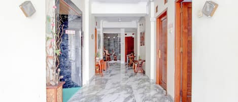 A hallway with marble flooring, wooden doors, and a dining area with tables and chairs.