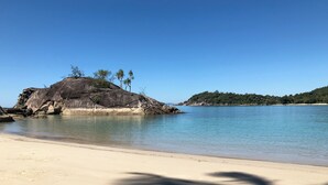 A beach with clear water, a sandy shore, and a large rock formation with trees.