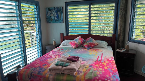 A neatly made bed with colorful bedding, a bedside table with a lamp, and a painting on the wall.