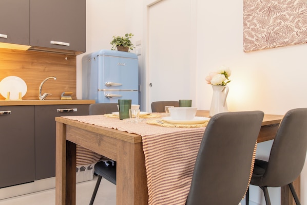 A modern kitchen with dark cabinets, a blue refrigerator, and a dining table set with plates, cups, and a vase of flowers. - La Corte - Monza Apartments (Monza)