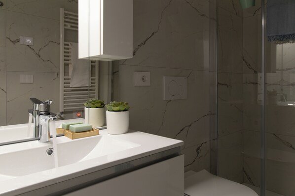 Une salle de bain moderne avec un lavabo blanc, un miroir, un porte-serviettes et une cabine de douche en verre.