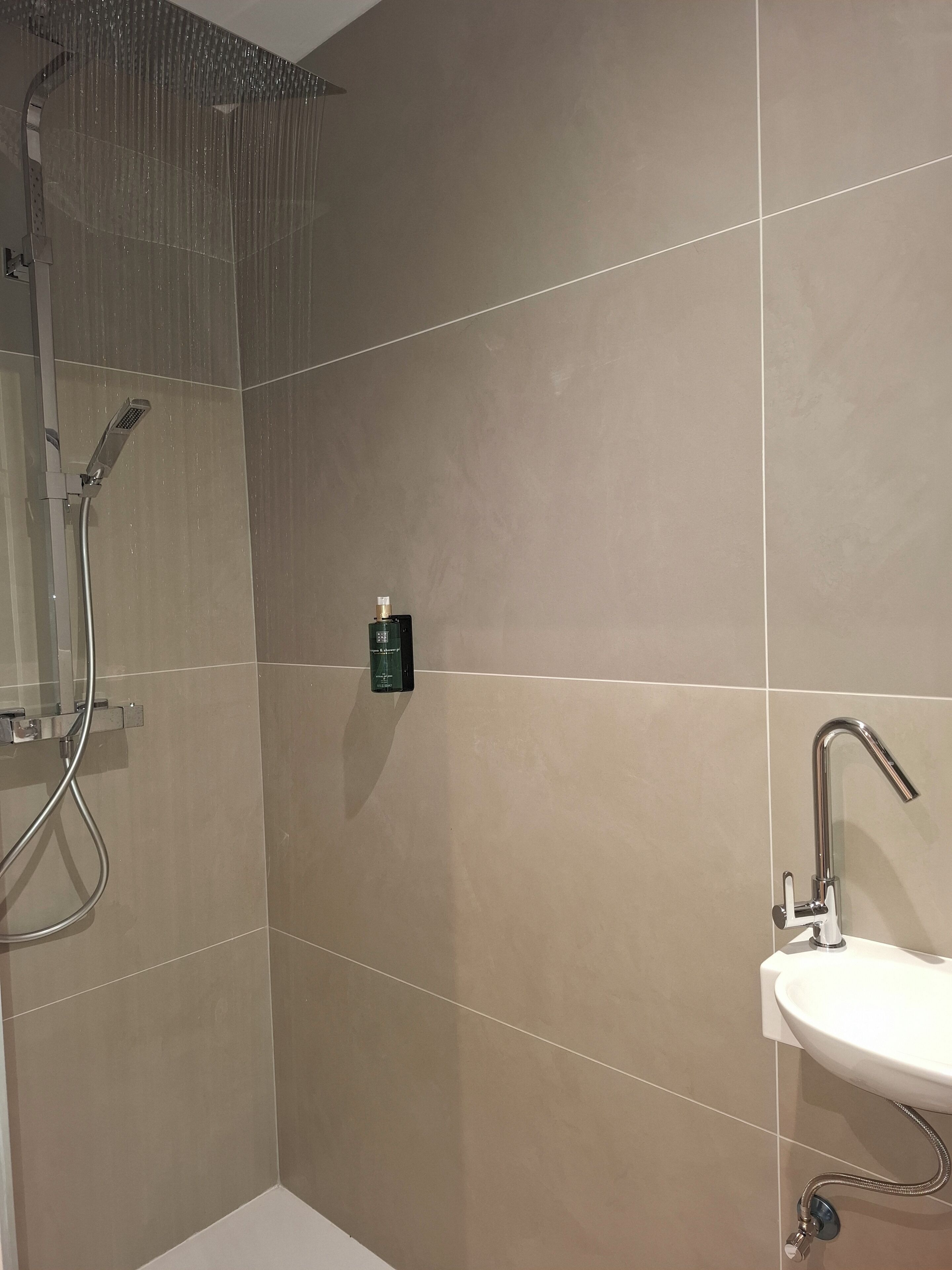 Un baño moderno con ducha acristalada, un cabezal de ducha de mano, un cabezal de ducha de mano, un grifo empotrado y un lavabo blanco.