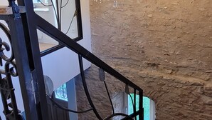 Un escalier avec une rampe en métal noir, un lustre et un mur au style rustique.