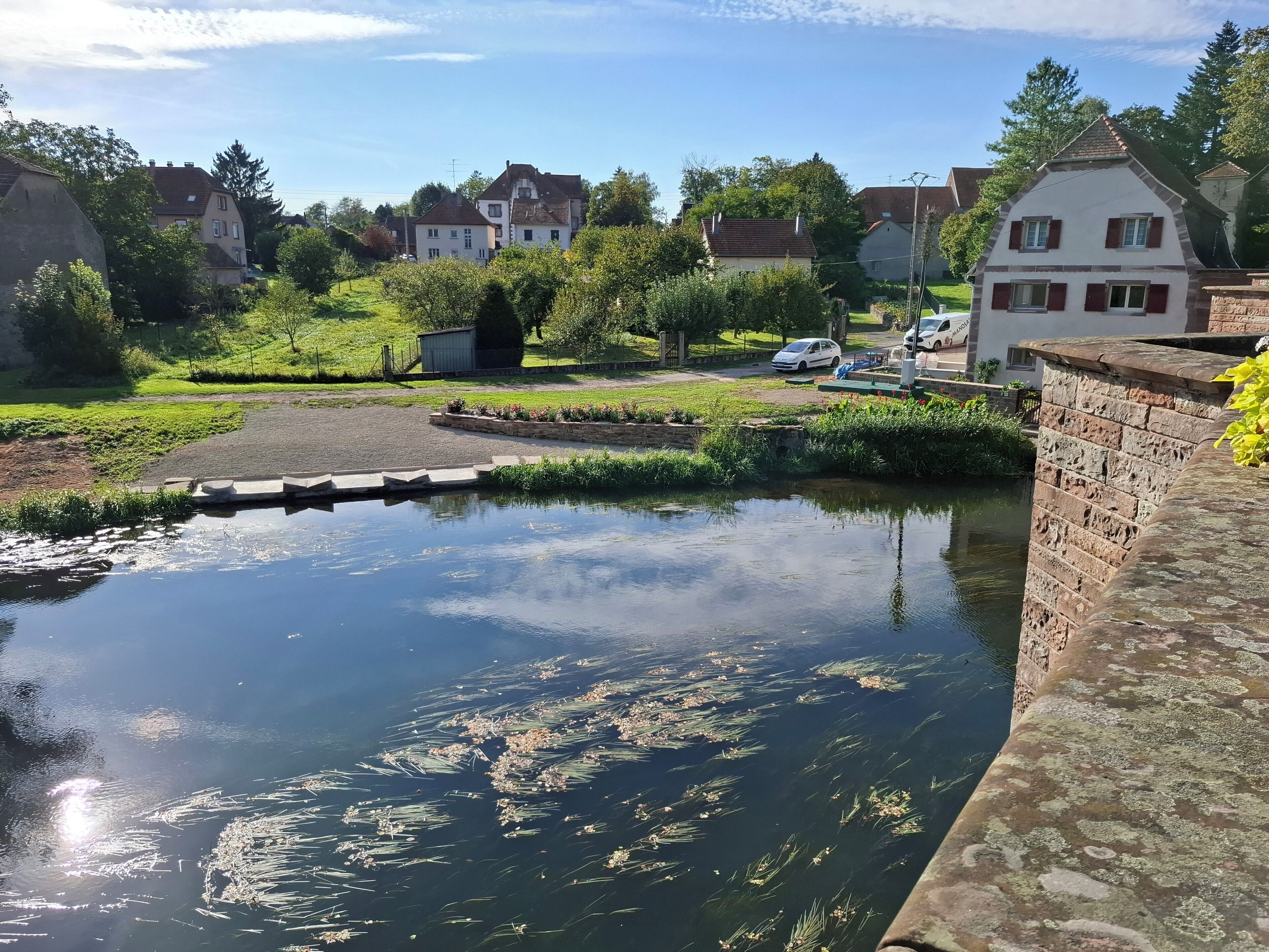 Una vista tranquilla lungo il fiume con un ponte, case e vegetazione.