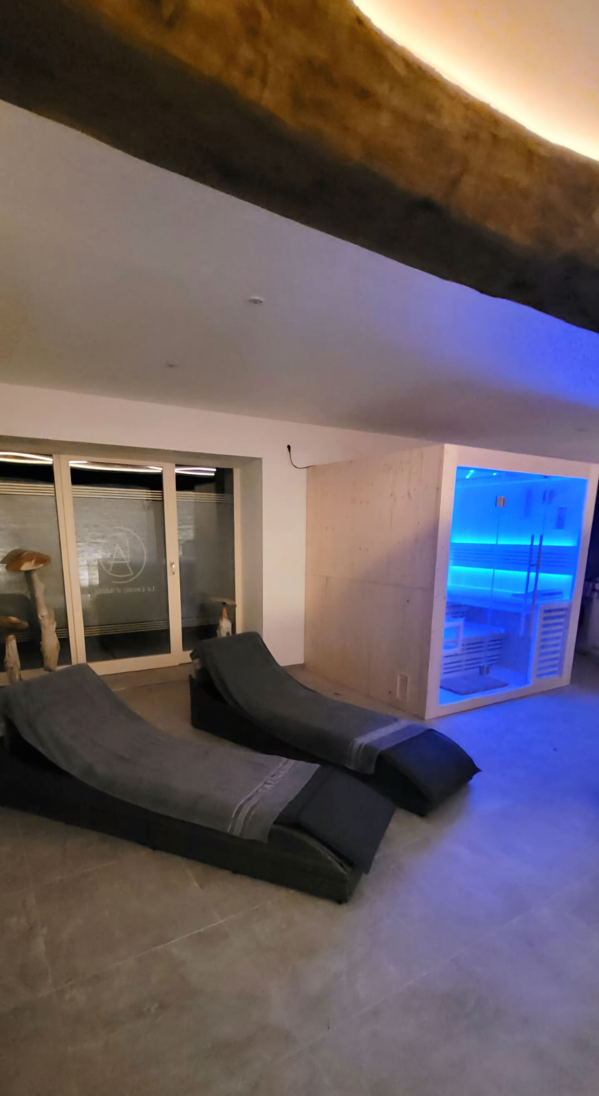 Een moderne kamer met twee fauteuils, een glazen deur naar een balkon en een gebied met blauwe verlichting.