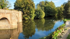 Une rivière avec un pont, de la verdure et une clôture rouge.