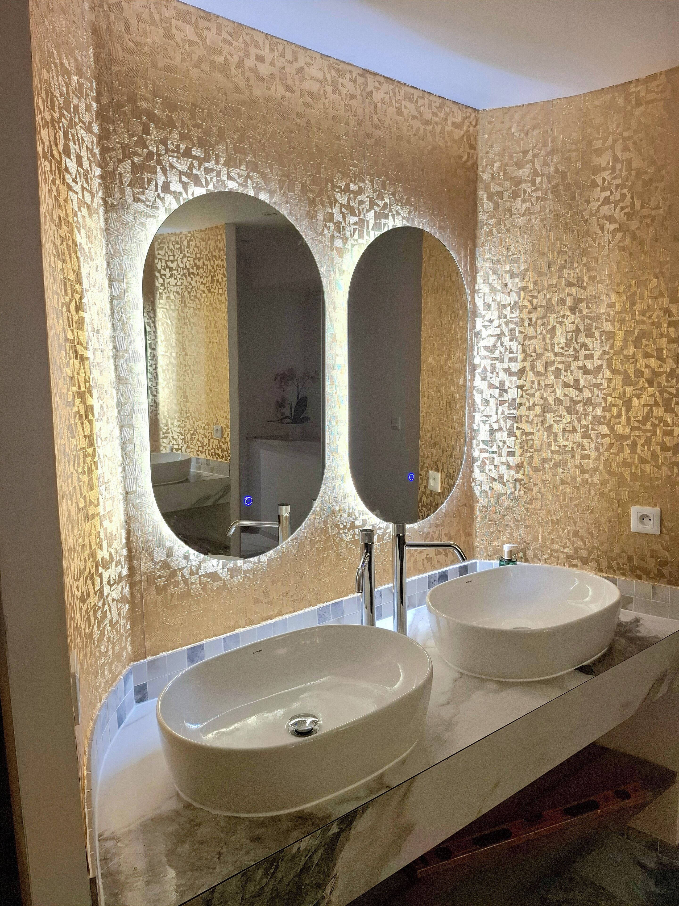 A bathroom with two round sinks, a large mirror, and a textured wall.