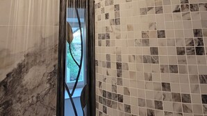 Une salle de bain moderne avec un mur en marbre, une porte en verre dotée d’un cadre métallique décoratif et une douche au plafond au design original.