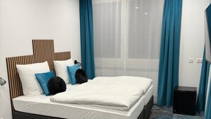 A modern hotel room with a large bed, blue curtains, and a view of the city. - Das Hartmanns (Pegnitz)