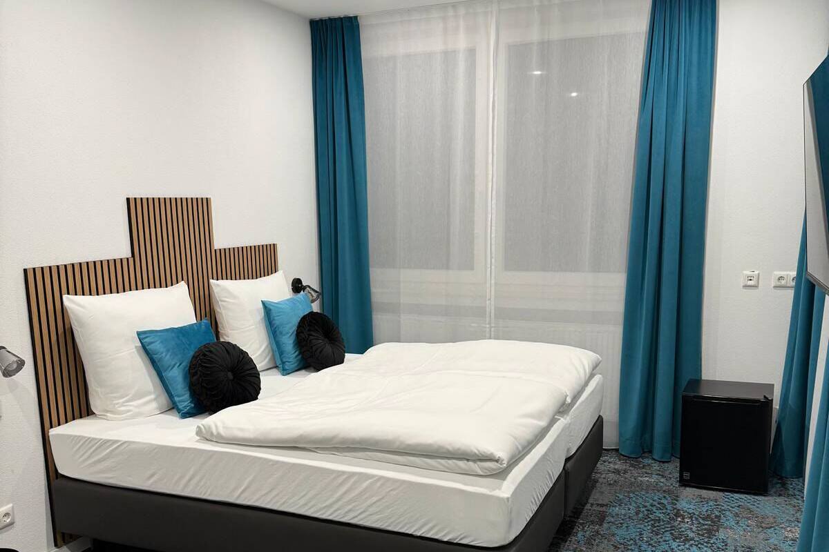 Ein modernes Hotelzimmer mit einem großen Bett, blauen Vorhängen und Blick auf die Stadt.