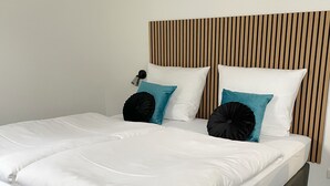 A bed with white bedding, two teal pillows, and a black accent pillow. The headboard has a vertical wooden panel design. - Das Hartmanns (Pegnitz)