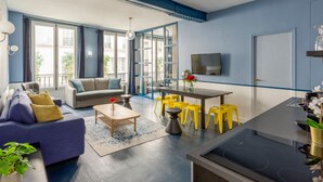 A modern living room with a sofa, coffee table, and yellow stools. There is a dining area with a table and chairs, and a kitchen with a stove. - Merveil Luxury Suite - Saint Denis I (Paris)