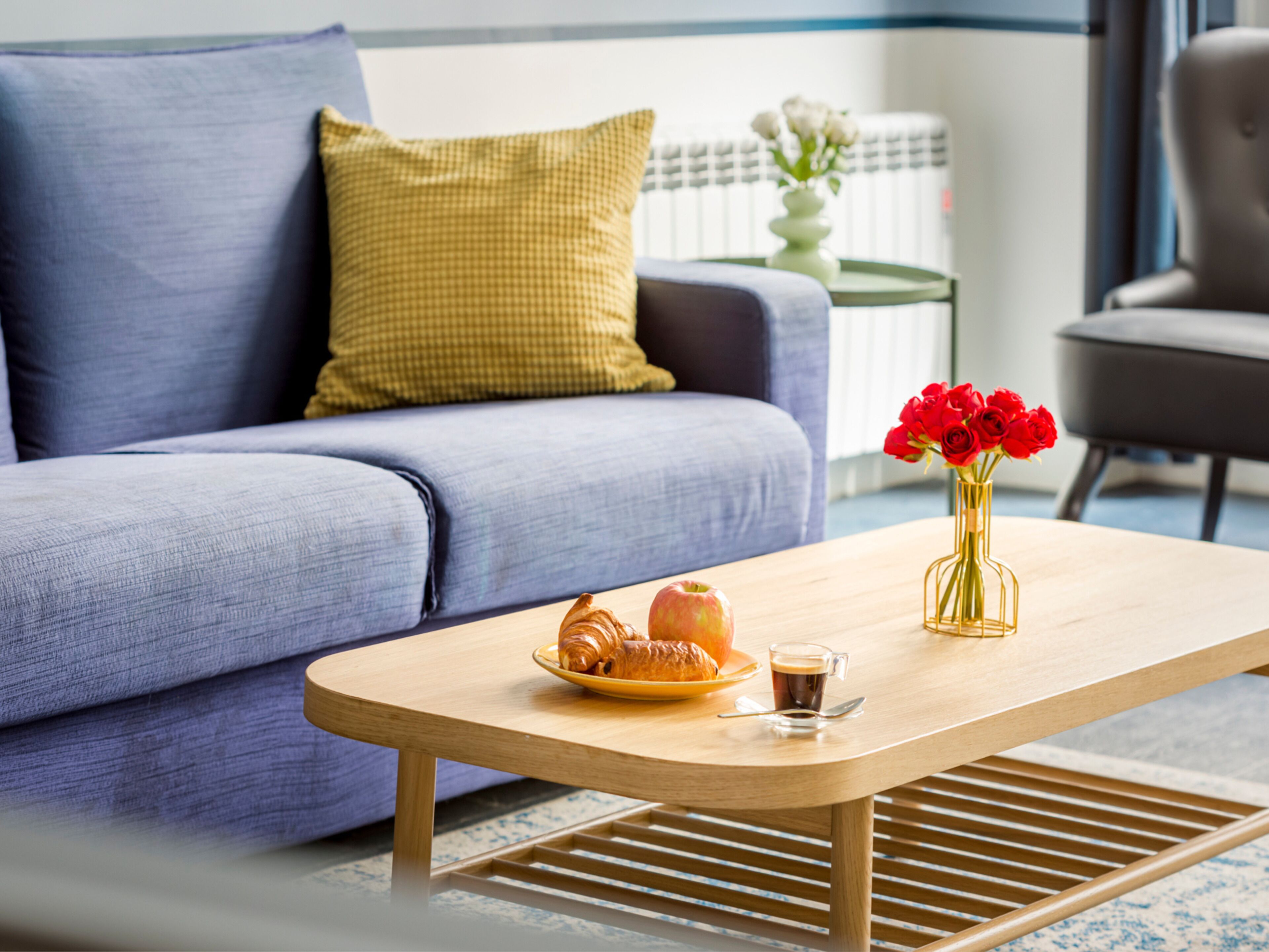 A modern living room with a sofa, a coffee table, and a vase with red flowers.