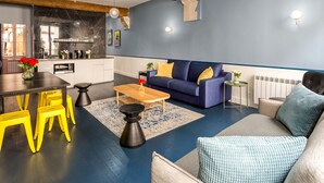 A modern living room with a blue sofa, yellow chairs, a wooden coffee table, and a kitchen in the background. - Merveil Luxury Suite - Saint Denis I (Paris)