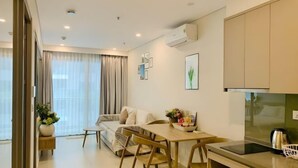 A modern kitchen with a dining area, a sofa, and a large window with curtains. - 2 Bedroom Luxury Condotel - The Song Vung Tau (Vung Tau)