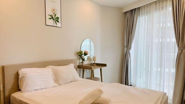 A neatly made bed with a rolled towel, a bedside table with a mirror, and a framed picture on the wall. - 2 Bedroom Luxury Condotel - The Song Vung Tau (Vung Tau)